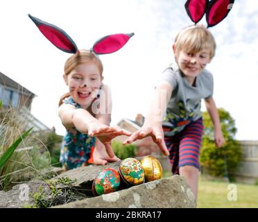 Un fratello e una sorella, indossando la pittura facciale e le orecchie conigliate fatte in casa, prendere parte a una caccia all'uovo di Pasqua la Domenica di Pasqua nel loro giardino. Foto Stock