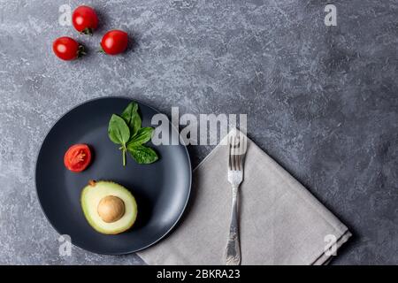 Piatto nero su fondo di pietra grigia con cibo per donne rosso cherrys pomodoro, spinaci e avocado Foto Stock