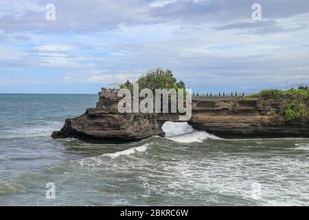 Le onde arrivano a una scogliera sotto il tempio di Batu Bolong. Tanah Lot tempio. Enorme buco nella roccia sotto il tempio pura Batu Bolong. Tempio indù sul BE Foto Stock