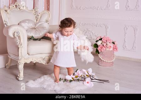 Un bambino di 1 anno come un angelo sorridere. Giornata internazionale dei bambini. Bambino in ali d'angelo in stile barocco camera interna. Foto Stock