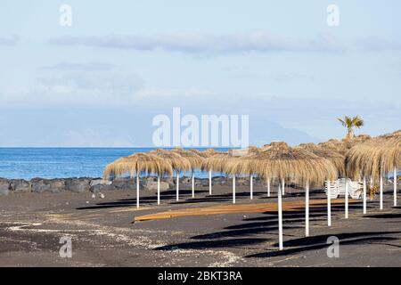Ombrelloni di paglia in paglia su una spiaggia deserta di Playa Beril durante il covid 19 lockdown nella zona turistica di Costa Adeje, Tenerife, Canar Foto Stock