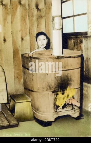 [ 1940 Giappone - bagno giapponese ] - un ragazzo che prende un bagno in una vasca di legno riscaldata dalla legna da ardere. cartolina vintage del xx secolo. Foto Stock