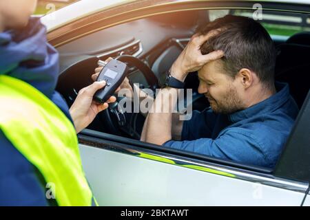 concetto di drink e drive - triste ubriaco uomo seduto in auto dopo la polizia prova di alcol con alcometer Foto Stock