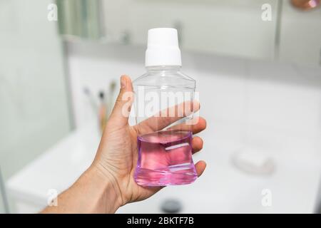 Mano che tiene il collutorio blu in un bagno. Foto Stock