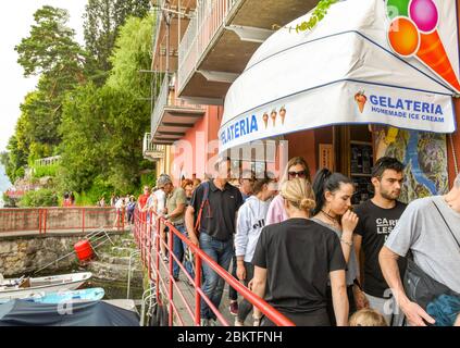 VARENNA, LAGO DI COMO, ITALIA - 2019 GIUGNO: Si spreme lungo la stretta passerella passando davanti a una gelateria nel porto nel villaggio di Varenna Foto Stock