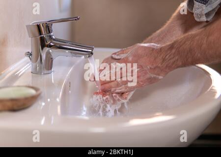 Giovane uomo caucasico lavando le mani sfregando con sapone sotto il rubinetto d'acqua corrente nel bagno. Igiene personale e assistenza sanitaria per la prevenzione delle malattie Foto Stock