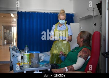 Un membro del personale clinico indossa i dispositivi di protezione individuale (PPE), perché si prende cura della paziente Trudy Woodfall che si sta riprendendo dal coronavirus nel Covid Recovery Ward presso il Royal Papworth Hospital di Cambridge. Foto Stock