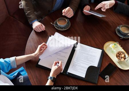 Sopra la vista di businesswoman irriconoscibile che firma il contratto dopo la trattativa con i soci di affari in caffè Foto Stock