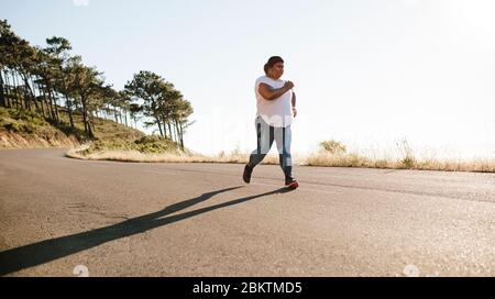 Donna sana che corre al mattino su una strada. Jogging femminile in sovrappeso all'aperto al mattino. Foto Stock