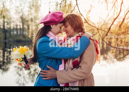 Giorno della madre. Madre anziana con fiori dotati e la sua figlia adulta abbracciare dal fiume primavera. Valori familiari Foto Stock