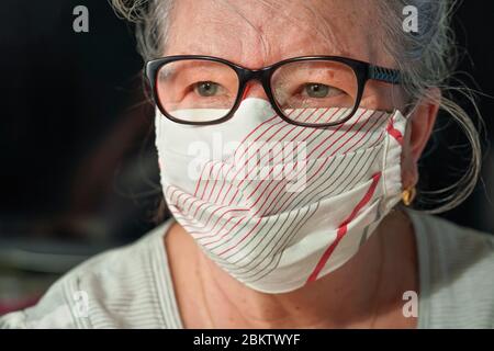 Anziana donna anziana con occhiali che indossano mano fatto bocca naso naso virus maschera viso. Concetto di prevenzione delle epidemie di coronavirus covid-19 Foto Stock