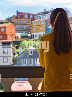 Giovane donna che le ha aggrappato le mani sul balcone per showi gratitudine a tutti gli operatori sanitari durante l'epidemia di coronavirus. Molte case colorate. Foto Stock