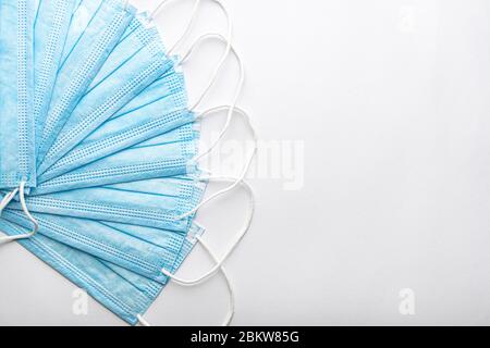 Diverse maschere di protezione monouso blu medico una sopra l'altra sotto forma di ventilatore su sfondo bianco. Medicazione chirurgica chiude bocca e naso Foto Stock