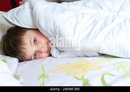 Vista dall'alto del ragazzino a letto che copriva il viso con coperta bianca o copriletto. Ragazzo che dorme. Foto Stock