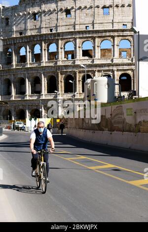 L'uomo che indossa una maschera medica, in bicicletta, passa davanti al Colosseo durante il blocco per Coronavirus Covid 19. Roma, Italia, Europa, UE. Foto Stock