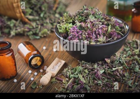 Bottiglie di globules omeopatici. Origanum vulgare o fiori di maggiorana selvatici in ciotola. Bottiglia di olio essenziale o infusione ed erbe medicinali su backgro Foto Stock