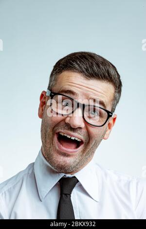 Uomo d'affari ridente e divertente con faccia rasata, occhiali e camicia bianca. Primo piano in studio con testa frontale ritratto contro il retro luminoso Foto Stock