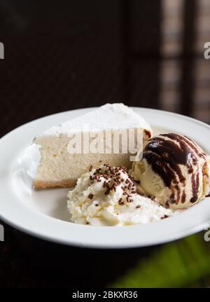 Una fetta di torta al formaggio con gelato e panna montata su un piatto bianco. Foto Stock