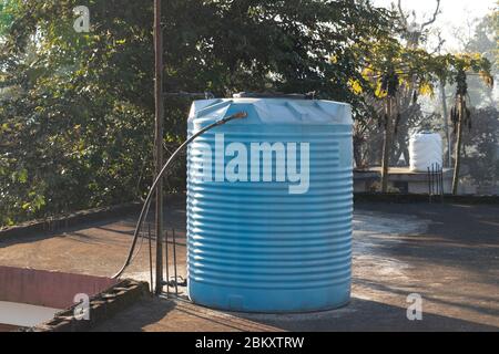 Serbatoio dell'acqua blu posto sulla terrazza della casa collegata con tubi in acciaio. Foto Stock