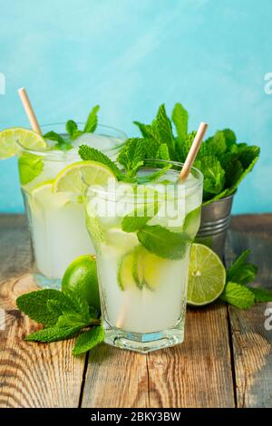 Due limonate o mojito fatti in casa cocktail con lime, menta e ghiaccio cubetti in un bicchiere su un tavolo rustico in legno. Drink estivo fresco. Foto Stock