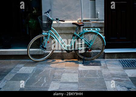 Bicicletta blu città con un cesto in piedi sulla vecchia strada con mattoni quadrati vicino all'edificio. Foto Stock