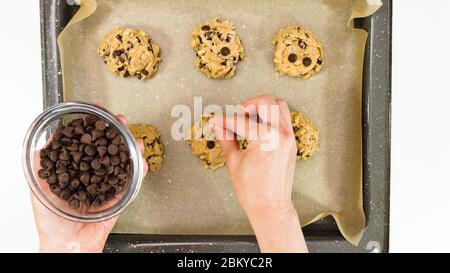 Ricetta di biscotti al cioccolato. Donna che mette i trucioli di cioccolato sulla parte superiore dei biscotti non cotti, primo piano, vista dall'alto Foto Stock