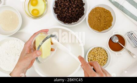 Ricetta dei biscotti del chip del cioccolato. Chef mettere il burro in un ciotola.Chocolate chips, noci, e alcuni altri ingredienti per cuocere esigenze primo piano su kit bianco Foto Stock