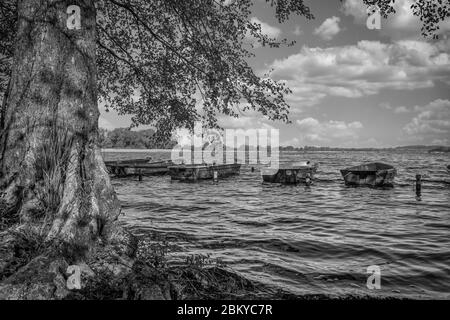 diverse piccole barche a remi sono ormeggiate fianco a fianco al bordo di un lago Foto Stock