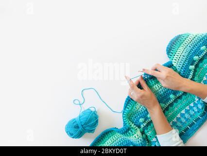 Le mani delle donne sono grandi. Donna crochets. Filati di colore verde, turchese, acquamarina e blu. Sfondo in legno bianco. Foto Stock