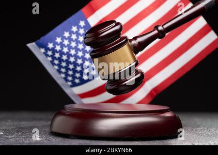 Primo piano del simbolo del diritto e della corte. Gavel di legno sullo sfondo della bandiera americana su sfondo nero in studio Foto Stock