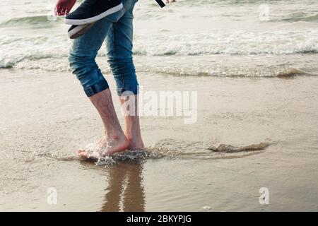 Le gambe dell'uomo a piedi nudi camminano sulla spiaggia di sity europea e godono di mare. Foto Stock