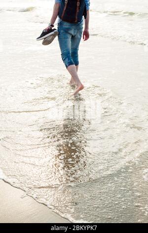 Le gambe dell'uomo a piedi nudi camminano sulla spiaggia di sity europea e godono di mare. Foto Stock