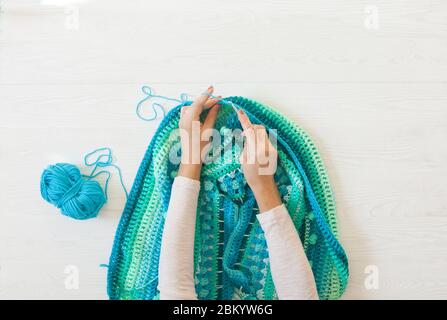 Le mani delle donne sono grandi. Donna crochets. Filati di colore verde, turchese, acquamarina e blu. Sfondo in legno bianco. Foto Stock