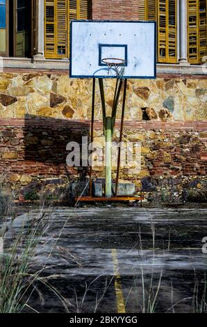 Il vecchio cerchio di basket sta lentamente decadendo dietro il vecchio edificio di appartamenti abbandonati. Foto Stock