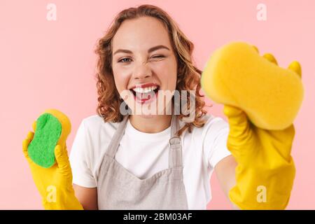 Foto di felice donna donna casalinga positiva isolato su sfondo rosa parete in guanti tenendo spugne guardando la macchina fotografica. Foto Stock