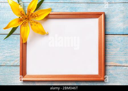 Cornice in legno marrone con fiori gialli giglio su vecchio sfondo blu shabby con spazio copia. Biglietto di auguri floreale, piatto. Foto Stock