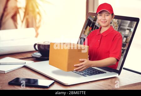 Donna asiatica consegna in camicia rossa con sfondo sfocato magazzino, tenere ordine merci in pacco fuori dal computer portatile. Ordinare online e del Foto Stock