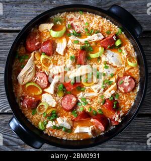 Succosa pog di pollo meridionale con carne di pollo, riso, salsiccia affumicata, porro cotto con brodo di pollo servito su un piatto nero su sfondo di legno, vi Foto Stock