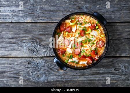 Piatto di pollo con carne di pollo, riso, salsiccia affumicata, porro cotto con brodo di pollo su un piatto nero su sfondo di legno, vista dall'alto, copia Foto Stock