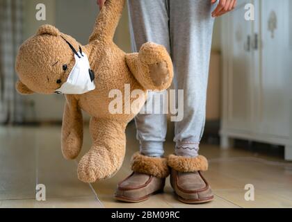 Ragazza adolescente che abbrutono orso di teddy con maschera facciale. Concetto di virus corona, rimanere a casa, isolamento. Prevenzione del virus influenzale Foto Stock