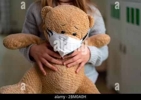 Ragazza adolescente che abbrutono orso di teddy con maschera facciale. Concetto di virus corona, rimanere a casa, isolamento. Prevenzione del virus influenzale Foto Stock