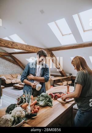 Coppia giovane amorevole che taglia insieme le verdure nella cucina rustica Foto Stock