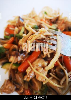 Pasta con verdure, funghi e pollo su una piastra bianca. Pasta cinese,fritto soba noodles con funghi, carote, peperoni closeup su bianco plat Foto Stock