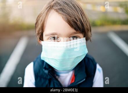 Bambino che indossa maschera medica durante la pandemia Coronavirus COVID-19. Primo piano e contatto visivo con lo spettatore. Ritorno a scuola, Nuova realtà e prevenzione Foto Stock