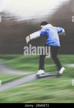 Vista posteriore di un giovane inriconoscibile e sfocato in abbigliamento sportivo con skateboard nel parco estivo Foto Stock