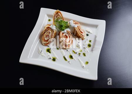 Vista dall'alto di quattro panini a fette con pasta e salmone serviti con rucola per insalata, pesto e panna acida su piatto bianco. Piatto gustoso isolato su legno nero Foto Stock