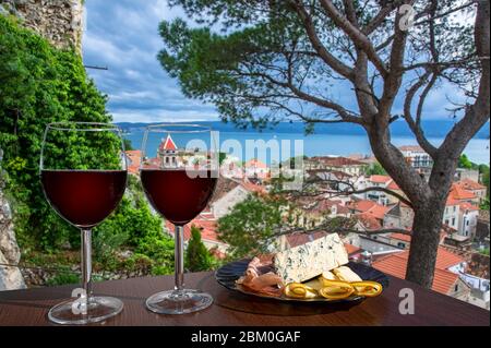 Due bicchieri di vino rosso con assortimento di salumi con vista sulla città croata di Omis con tetti rossi e mare blu. Bicchiere di vino rosso con spuntini. Foto Stock