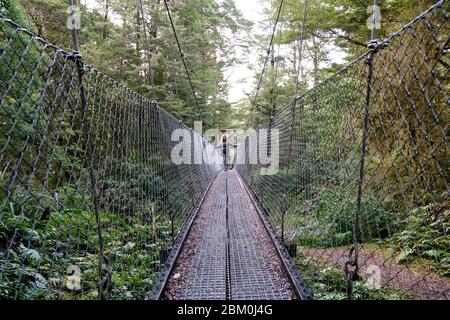 Donna che attraversa un ponte sospeso su un ruscello sulla pista Kepler. Foto Stock