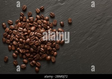 Mucchio di chicchi di caffè appena tostati su un ardesia di pietra grigia Foto Stock