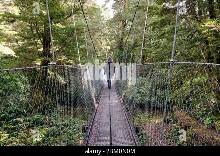 Donna che attraversa un ponte sospeso su un ruscello sulla pista Kepler. Foto Stock